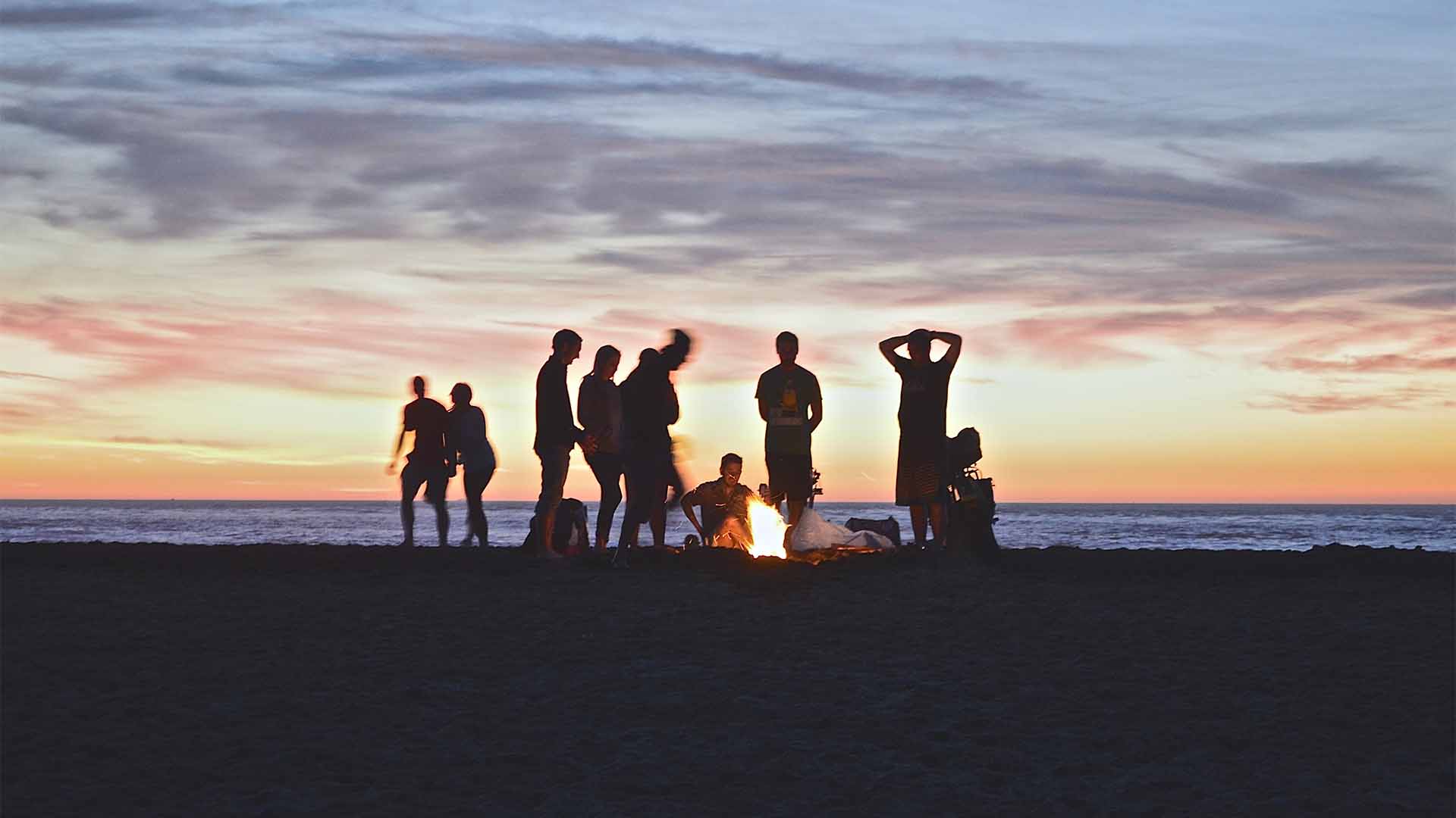 Backpacker stehen am Strand um ein Lagerfeuer
